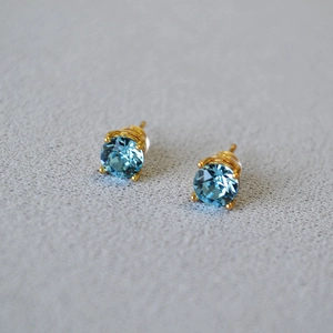 Macro shot of light blue round crystal earrings with gold four-prong setting and 925 silver pins