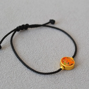 Detail of adjustable black woven rope bracelet with gold enamel floral charm