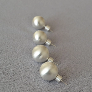 Détail de quatre boucles d'oreilles boules argent mat avec finition brossée sur tissu