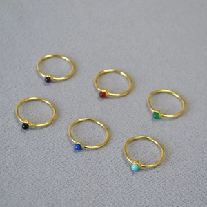 Macro detail of six minimalist gold brass rings featuring small colorful gemstone beads