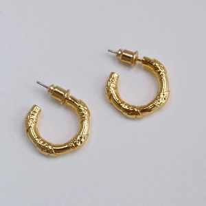 Macro detail of gold plated C-shaped earrings with hammered metal texture and stud back
