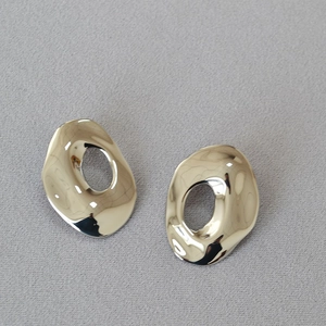 Macro shot of silver textured irregular oval hollow earrings on grey fabric background