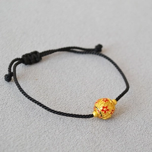 Close-up of a handmade black braided bracelet with an enamel flower brass bead
