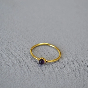 Minimalist gold brass ring with a round purple stone inlay on a grey textured surface