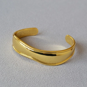 Macro detail of wave-shaped polished gold brass cuff bracelet with smooth curved lines