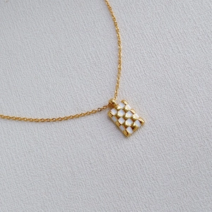 Détail du collier en laiton plaqué or avec pendentif rectangulaire émaillé à carreaux dorés