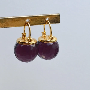 Detail of gold brass earring hooks with faceted purple beads and heart-engraved caps