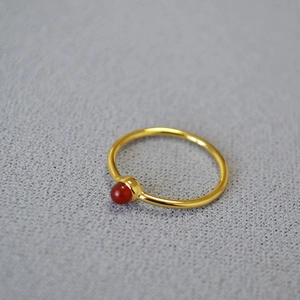 Close-up of minimalist thin gold-plated ring featuring a small round red agate gemstone