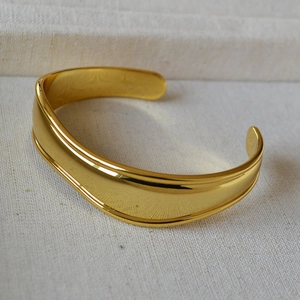 Macro shot of minimalist gold-plated wide cuff bracelet with polished concave design