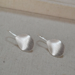 Close-up of silver brushed texture petal earrings on a neutral linen fabric background