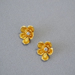 Detail of gold floral stud earring with brushed metal petals and a clear center gemstone