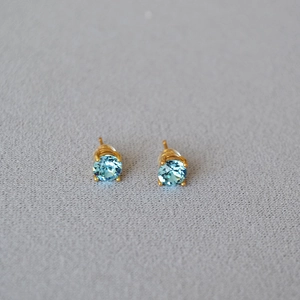 Detailed view of light blue round-cut crystal stud earrings with gold claw settings