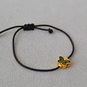 Macro shot of an adjustable black cord bracelet with a vintage gold butterfly charm