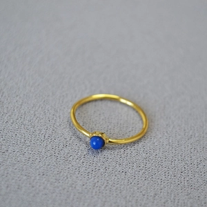 Minimalist gold plated brass ring with lapis lazuli stone set on grey background