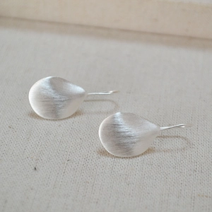 Detailed macro view of brushed silver leaf earrings with minimalist matte texture finish