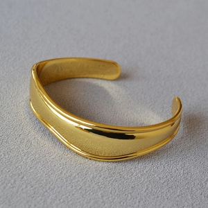 Detail of minimalist gold-plated irregular open cuff bracelet with mirror finish