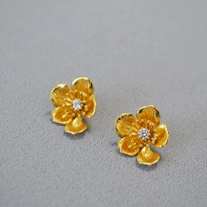 Detailed close-up of golden flower stud earrings with matte texture and central zircon stone