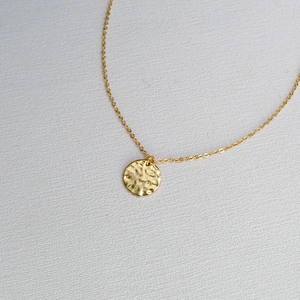 Détail d'un collier minimaliste plaqué or avec un pendentif à texture martelée unique