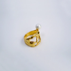 Détail macro d'une bague en laiton doré à texture irrégulière et perle blanche