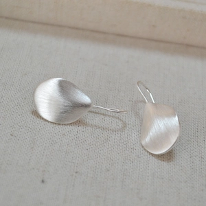 Close-up of irregular matte silver leaf earrings with brushed texture on linen fabric