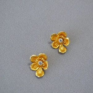 Detail of vintage gold flower stud earrings with matte texture and sparkling center zircon