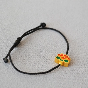 Detail of hand-woven black cord bracelet with colorful enamel lotus flower charm