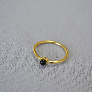 Close-up of a minimalist gold ring featuring a small round black stone on grey background