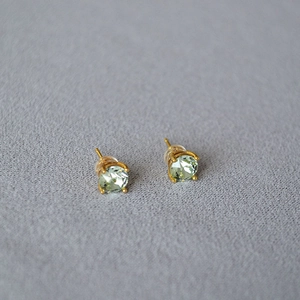 Detail of mint green crystal earrings with gold four-prong setting on grey fabric