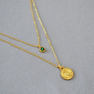 Detailed close-up of double-layered gold necklace with green gemstone and coin pendant