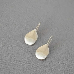 Macro detail of silver teardrop earrings featuring a brushed metal matte texture