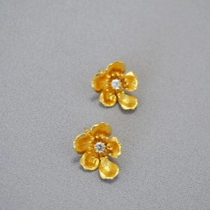 Macro detail of gold flower earrings with brushed texture and sparkling center stone