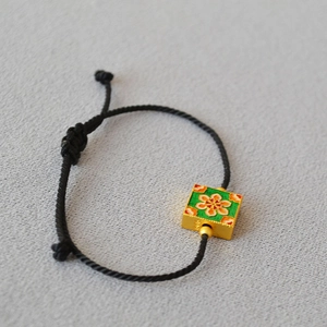 Macro shot of green enamel floral square charm on adjustable black braided cord bracelet