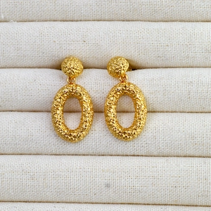 Close-up of gold-plated brass drop earrings with vintage hammered texture and oval design