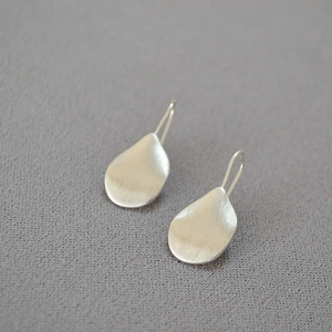 Detail view of silver drop earrings with brushed metal texture on grey fabric