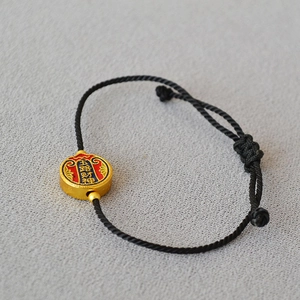 Detail of black woven rope bracelet featuring a golden enamel pendant with Five Wealth Gods text