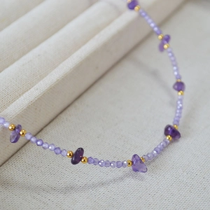 Elegant beaded necklace with irregular purple amethyst stones and gold accents on fabric