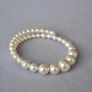 Detail of multi-layer faux pearl bracelet with gradient bead sizes on dark fabric