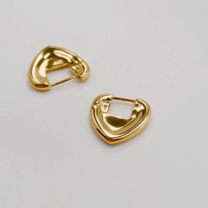 Detail of chunky gold-plated heart-shaped huggie earrings with a polished mirror finish