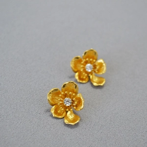Detailed close-up of golden floral earrings featuring intricate textures and central crystals