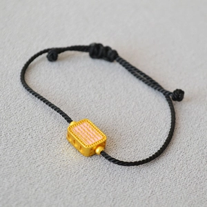 Detail of adjustable black woven bracelet with engraved gold rectangle bead and pink enamel