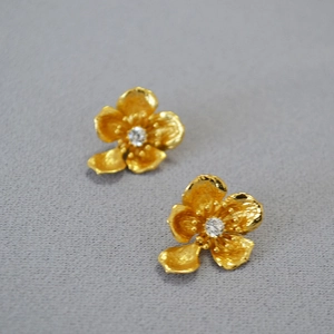 Macro detail of gold-plated petal earrings with matte texture and center stone