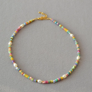 Bohemian choker necklace with colorful disk beads and white baroque pearls on grey surface