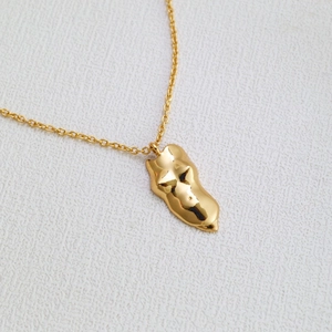 Gros plan sur un pendentif sculpture corps de femme doré sur une fine chaîne minimaliste