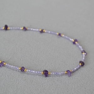 Macro shot of irregular amethyst beads and faceted purple stones on a golden beaded chain