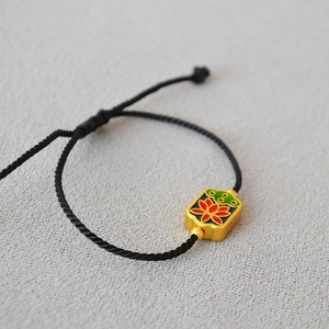 Detail of a black woven rope bracelet with a gold enamel lotus pendant and adjustable cord