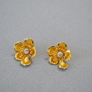 Detailed macro view of gold-plated petal earrings with crystal inlay on grey texture