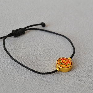 Detail of black woven rope bracelet with gold floral enamel pendant and adjustable knot