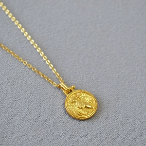 Detail of vintage brass coin pendant necklace with embossed deer motif and gold finish