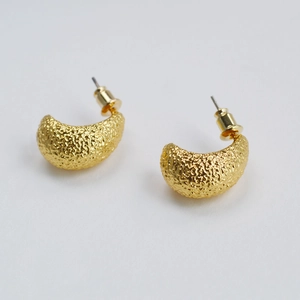 Macro shot of gold brass C-shaped stud earrings with hammered lava texture surface