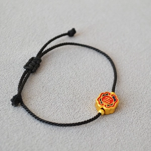 Detail of hand-woven black cord bracelet with vintage floral enamel gold charm